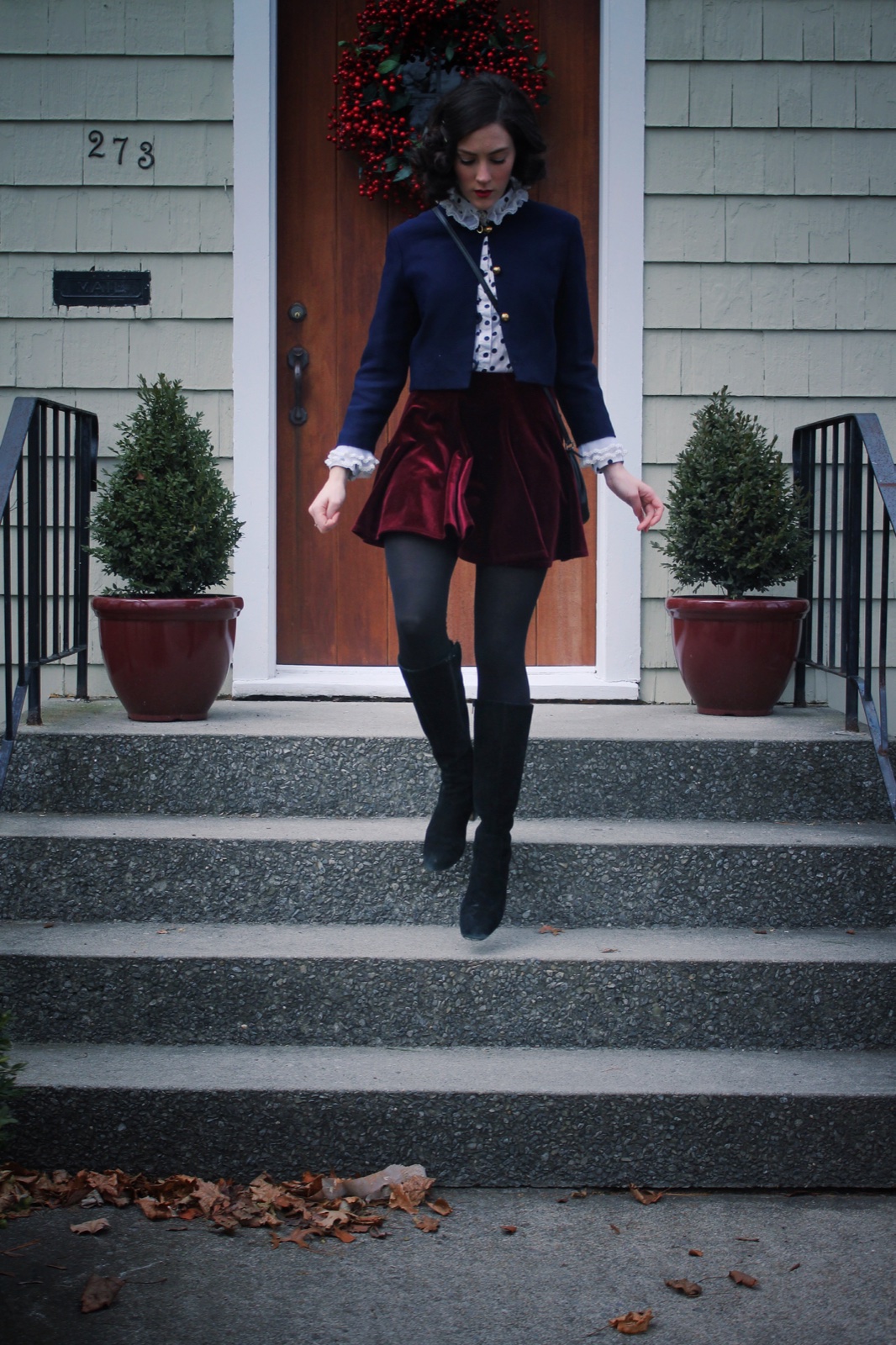 Young woman wearing a cropped navy military-inspired jacket with gold buttons, a velvet mini skirt, tights and boots in 2014