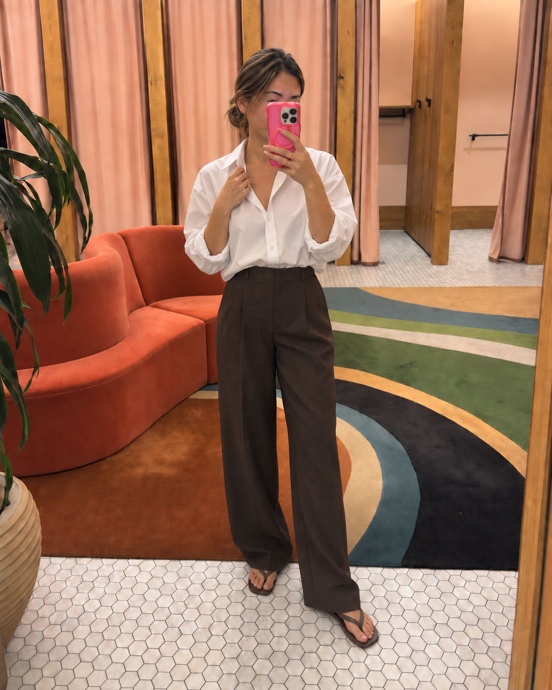 Jenni taking a mirror selfie in an Aritzia fitting room wearing a relaxed white poplin shirt, wide-leg cocoa trousers and brown square-toe sandals.