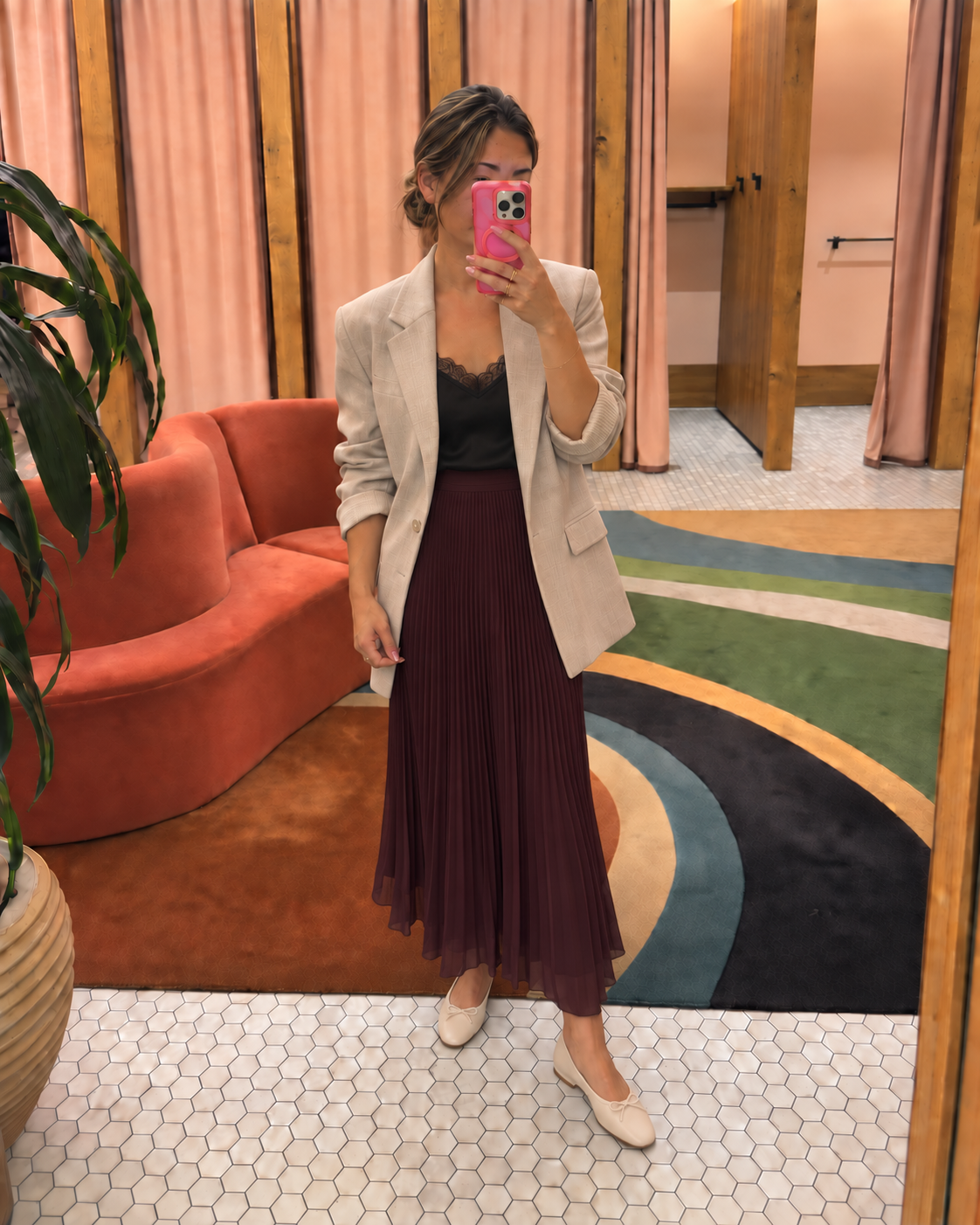Jenni taking a mirror selfie in an Aritzia fitting room wearing a cream blazer, black lace-trim satin camisole, plum pleated midi skirt and cream ballet flats.