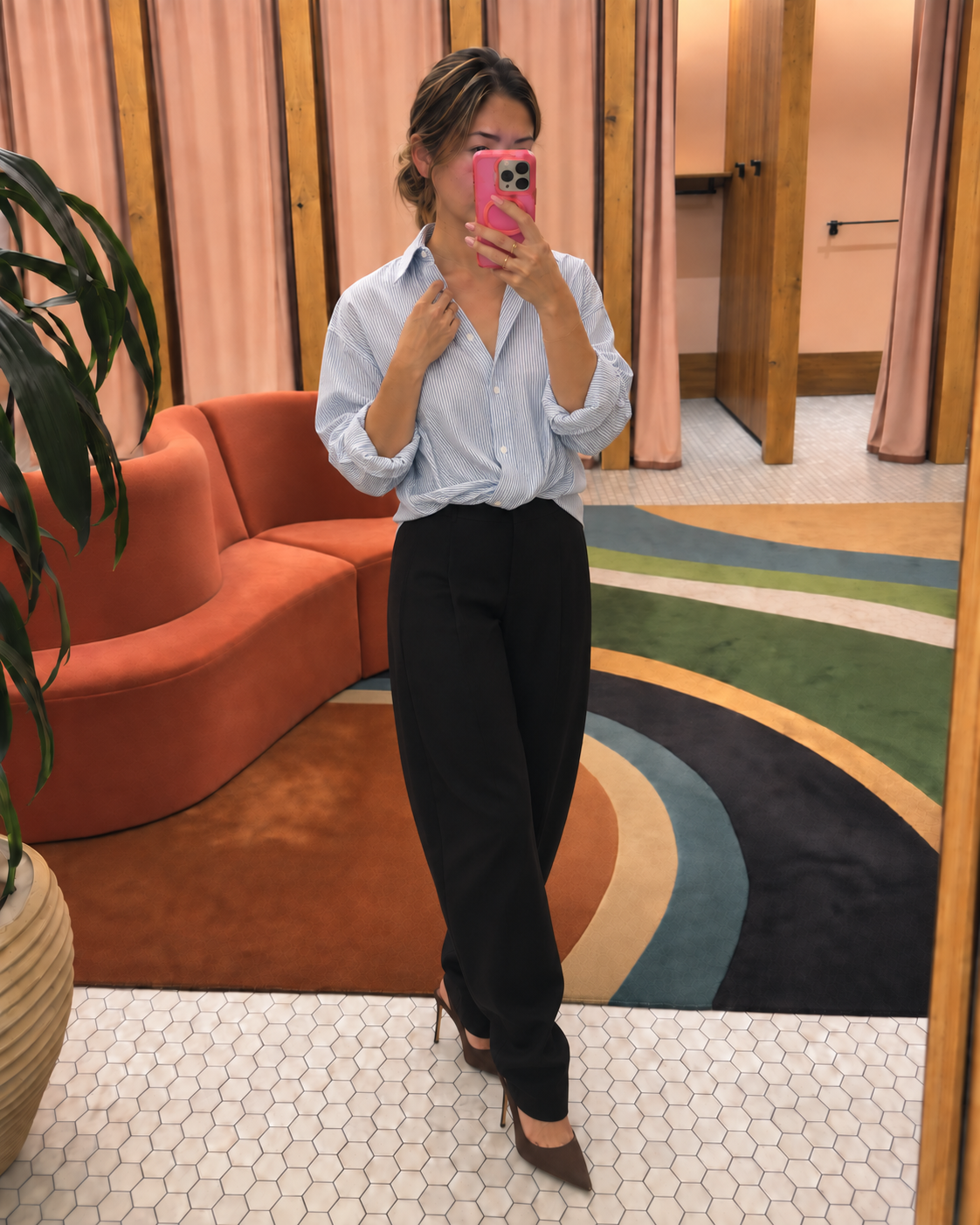 Jenni taking a mirror selfie in an Aritzia fitting room wearing a blue-and-white striped button-up shirt, black barrel pants and espresso pointed-toe heels.